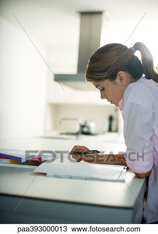 Stock Image - Teen girl doing homework in kitchen. Fotosearch