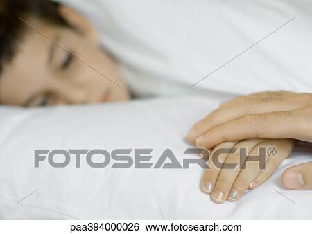 Child lying in bed, parent holding hand View Large Photo Image Stock Photograph - Child lying in bed, parent holding hand. Fotosearch