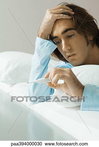 Man lying in bed, looking at thermometer View Large Photo Image Stock Image - Man lying in bed, looking at thermometer. Fotosearch