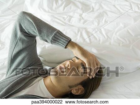 Man lying on bed, holding head View Large Photo Image Stock Image - Man lying on bed, holding head. Fotosearch