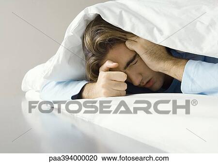 Man lying under covers, holding head View Large Photo Image Stock Image - Man lying under covers, holding head. Fotosearch