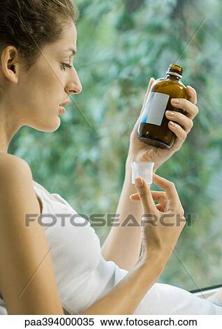 Stock Photography - Woman looking at bottle of cough syrup. Fotosearch