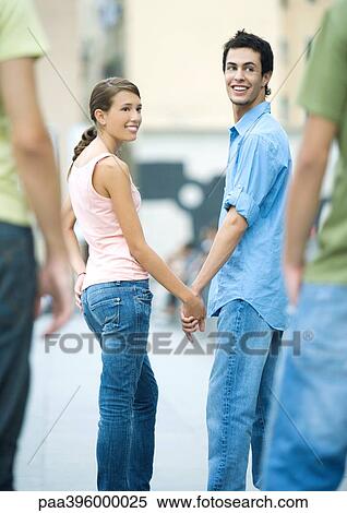 Teen couple holding hands, looking over shoulders at friends View Large Photo Image Stock Photography - Teen couple holding hands, looking over shoulders at friends. Fotosearch