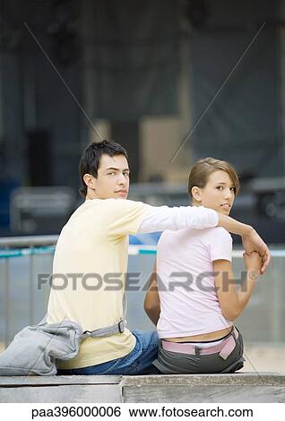Stock Photograph - Teen couple sitting, looking over shoulder. Fotosearch