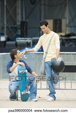 Teen males, one with skateboard the other holding helmet View Large Photo Image Picture - Teen males, one with skateboard the other holding helmet. Fotosearch
