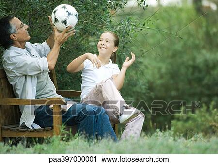 Stock Image - Girl and grandfather sitting together, playing with soccer ball. Fotosearch