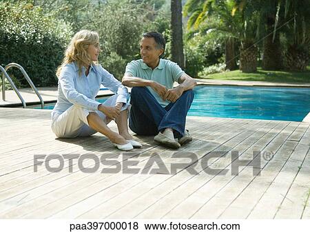 Mature couple sitting on deck by swimming pool View Large Photo Image Stock Photo - Mature couple sitting on deck by swimming pool. Fotosearch