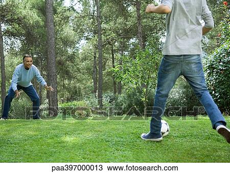 Stock Image - Mature man and teenage boy playing soccer. Fotosearch