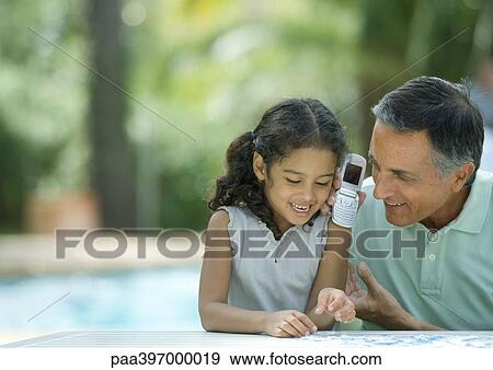 Mature man holding up cell phone to granddaughter's ear View Large Photo Image Stock Photo - Mature man holding up cell phone to granddaughter's ear. Fotosearch