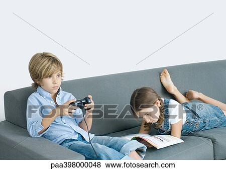 Boy sitting on sofa, holding joystick, girl next to him reading View Large Photo Image Stock Photo - Boy sitting on sofa, holding joystick, girl next to him reading. Fotosearch