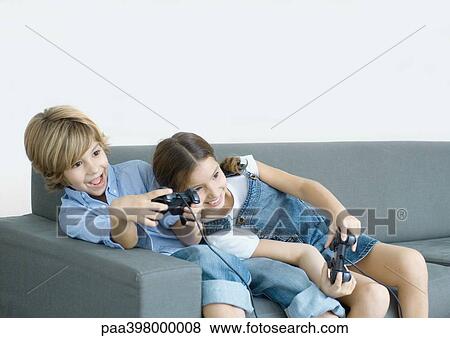 Stock Photo - Children sitting on sofa, holding joysticks. Fotosearch