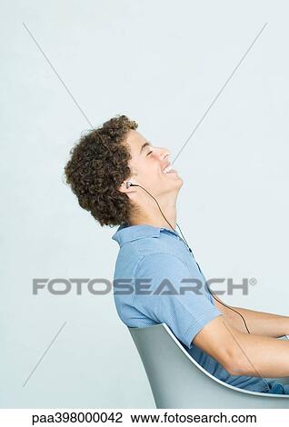 Man sitting in chair, listening to earphones, eyes closed, smiling View Large Photo Image Stock Image - Man sitting in chair, listening to earphones, eyes closed, smiling. Fotosearch