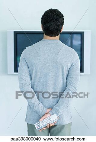 Man standing in front of widescreen TV, holding two remote controls, rear view View Large Photo Image Stock Image - Man standing in front of widescreen TV, holding two remote controls, rear view. Fotosearch