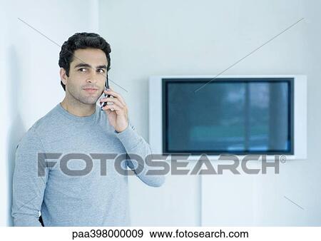 Stock Photo - Man using cell phone, widescreen TV in background. Fotosearch