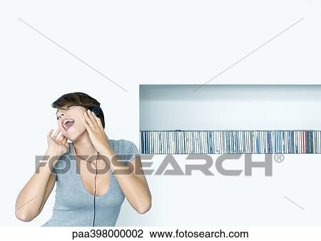 Woman listening to headphones, shelf of cds in background View Large Photo Image Stock Image - Woman listening to headphones, shelf of cds in background. Fotosearch