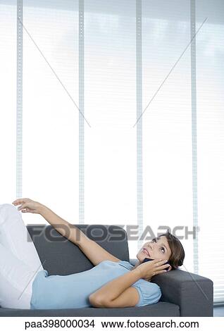Picture - Woman lying on sofa, using cell phone. Fotosearch