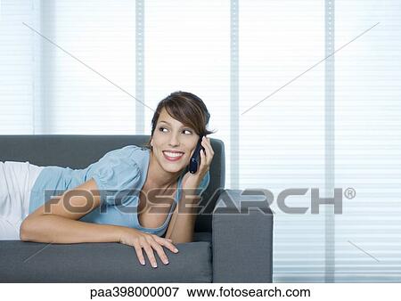 Stock Photo - Woman lying on sofa, using cell phone. Fotosearch