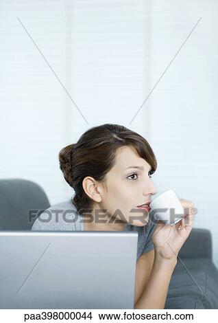 Woman using laptop and sipping coffee View Large Photo Image Picture - Woman using laptop and sipping coffee. Fotosearch