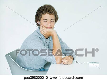 Young man sitting at table, listening to portable MP3 player View Large Photo Image Stock Image - Young man sitting at table, listening to portable MP3 player. Fotosearch
