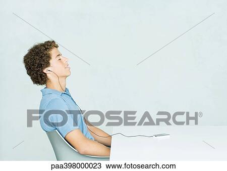 Young man sitting at table, listening to portable MP3 player View Large Photo Image Stock Image - Young man sitting at table, listening to portable MP3 player. Fotosearch