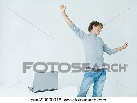 Young man standing, stretching, next to laptop View Large Photo Image Stock Photo - Young man standing, stretching, next to laptop. Fotosearch