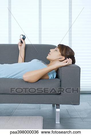 Young woman lying on sofa, listening to portable MP3 player View Large Photo Image Stock Photograph - Young woman lying on sofa, listening to portable MP3 player. Fotosearch