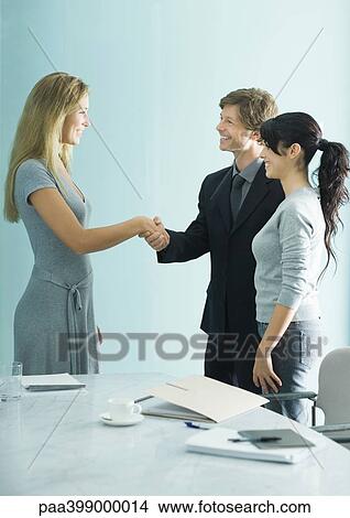 Businessman and woman shaking hands while casually dressed young woman stands by View Large Photo Image Picture - Businessman and woman shaking hands while casually dressed young woman stands by . Fotosearch