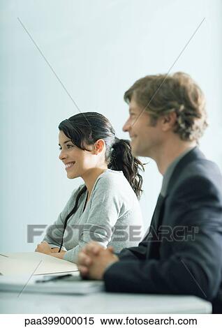Businessman and young woman sitting at table, looking out of frame View Large Photo Image Stock Photography - Businessman and young woman sitting at table, looking out of frame. Fotosearch