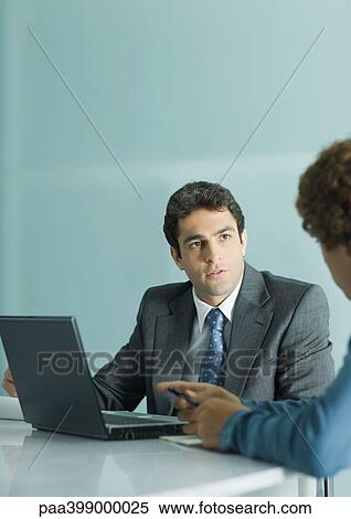 Businessman sitting at table, speaking to second man View Large Photo Image Stock Photography - Businessman sitting at table, speaking to second man. Fotosearch