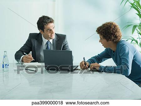 Businessman speaking to casually dressed young adult male, sitting at table View Large Photo Image Stock Photo - Businessman speaking to casually dressed young adult male, sitting at table. Fotosearch