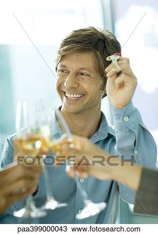 Stock Image - Glasses of champagne being clinked and man holding up keys, smiling. Fotosearch