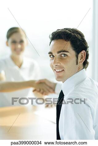 Man and woman shaking hands across table, man smiling over shoulder at camera View Large Photo Image Picture - Man and woman shaking hands across table, man smiling over shoulder at camera. Fotosearch