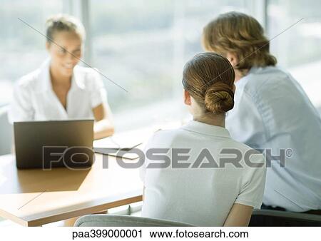 Man and woman sitting across table from smiling businesswoman, rear view View Large Photo Image Stock Image - Man and woman sitting across table from smiling businesswoman, rear view. Fotosearch