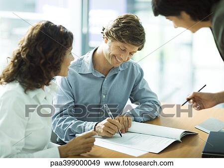 Man signing contract, smiling, while female partner and second woman watch View Large Photo Image Stock Photo - Man signing contract, smiling, while female partner and second woman watch. Fotosearch