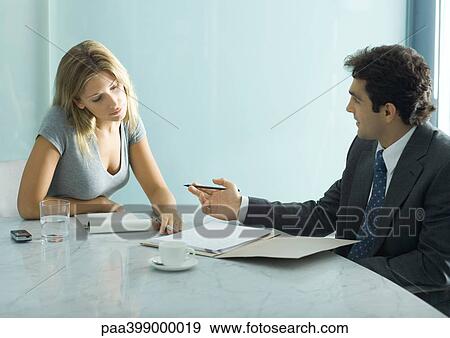 Stock Photo - Professional man and woman speaking and looking over document at table. Fotosearch