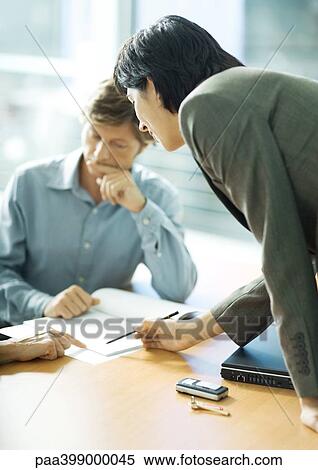 Professional woman leaning across table, pointing to document man is looking at View Large Photo Image Stock Photography - Professional woman leaning across table, pointing to document man is looking at. Fotosearch