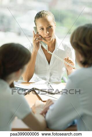 Stock Photography - Professional woman using phone, sitting across table from couple. Fotosearch