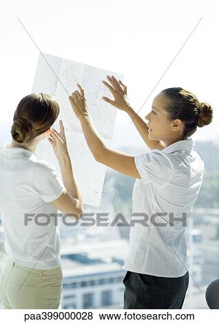 Stock Photo - Two professional women looking at blueprints and talking. Fotosearch