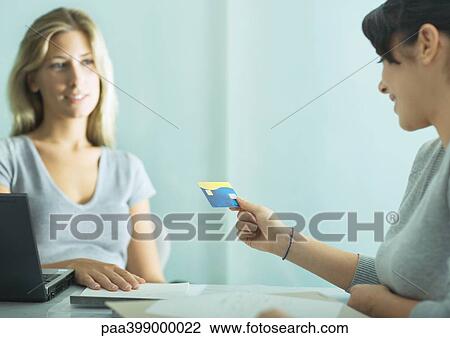 Two women sitting at table, one holding up card View Large Photo Image Stock Image - Two women sitting at table, one holding up card. Fotosearch