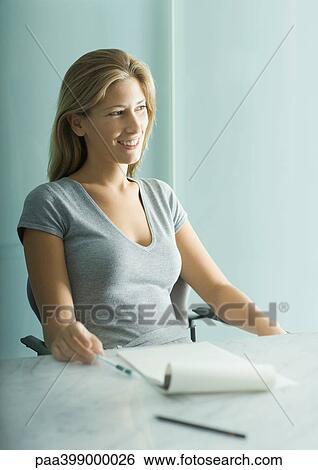 Woman sitting at table, notepad and pen on table View Large Photo Image Stock Photograph - Woman sitting at table, notepad and pen on table. Fotosearch