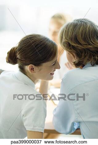 Young professional woman whispering to man, second woman in background View Large Photo Image Stock Photo - Young professional woman whispering to man, second woman in background. Fotosearch