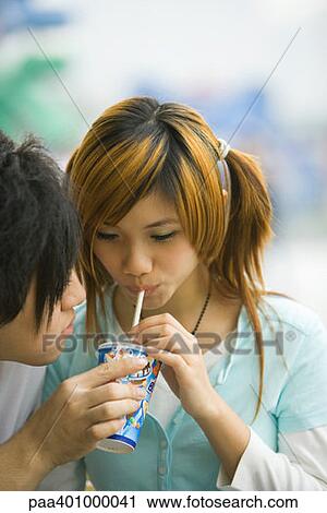Stock Image - Teenage couple, boy holding drink for girl . Fotosearch