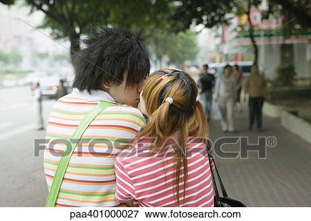 Stock Photo - Teenage couple kissing on sidewalk, rear view. Fotosearch