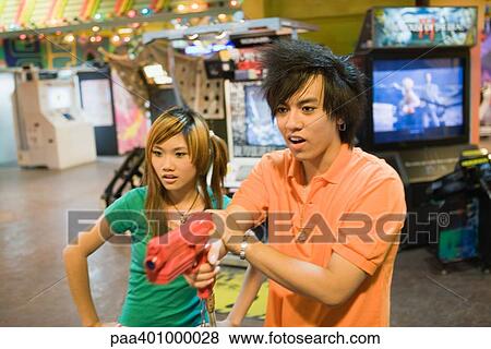 Stock Photo - Teenage couple playing game in video arcade. Fotosearch