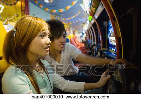 Stock Image - Teenage couple playing games in video arcade . Fotosearch