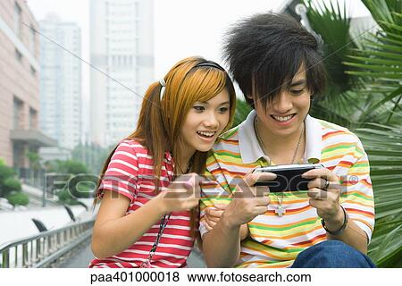 Teenage couple playing with handheld video game, outdoors View Large Photo Image Stock Photo - Teenage couple playing with handheld video game, outdoors. Fotosearch