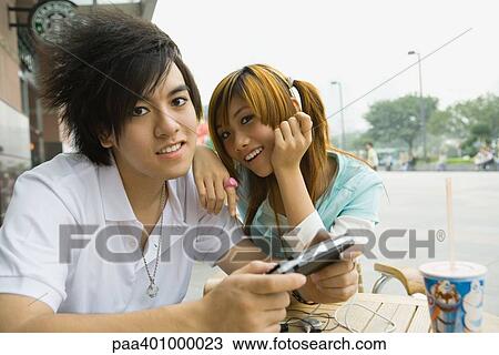 Teenage couple sitting at outdoor cafe, boy holding video game View Large Photo Image Stock Image - Teenage couple sitting at outdoor cafe, boy holding video game. Fotosearch