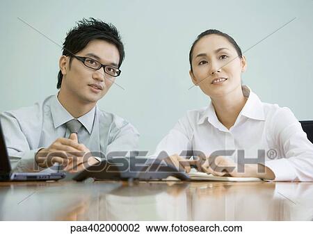 Stock Image - Businessman and woman sitting at table, looking up. Fotosearch