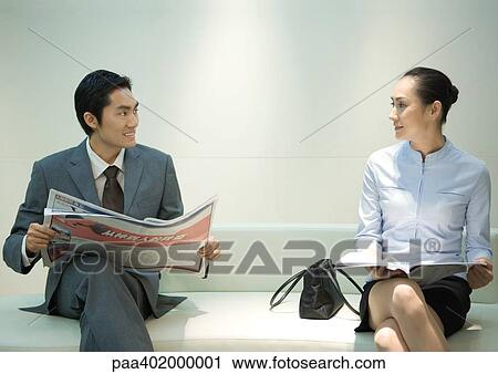 Businessman and woman sitting on waiting room bench, smiling at each other View Large Photo Image Stock Image - Businessman and woman sitting on waiting room bench, smiling at each other. Fotosearch
