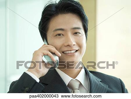 Stock Image - Businessman using cell phone, smiling at camera, portrait. Fotosearch